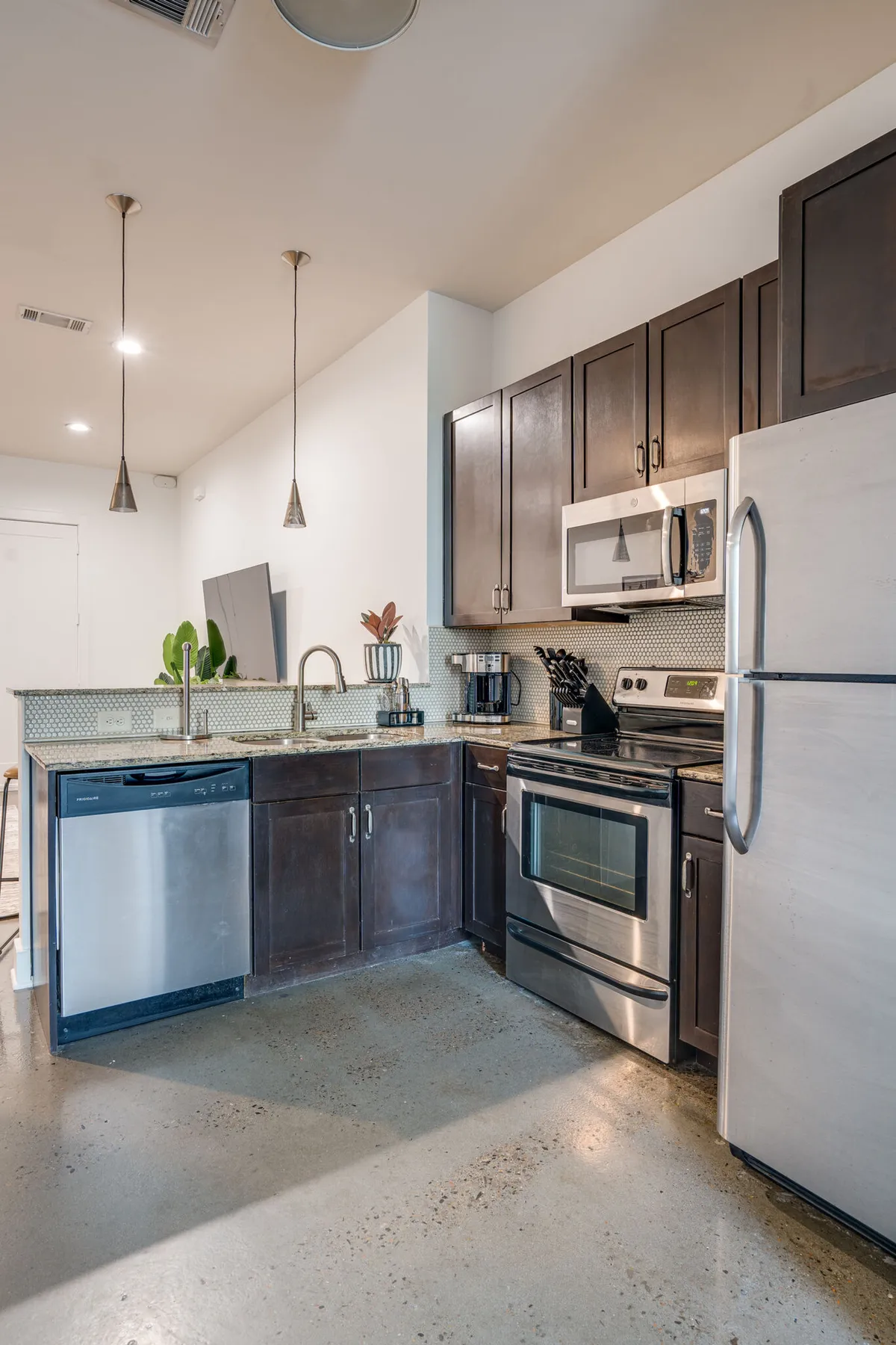 This image showcases a modern kitchen with sleek cabinetry, stainless steel appliances, and a granite countertop. A simple decorative plant adds a touch of warmth and homeliness. The space feels clean, functional, and inviting—ready for cooking, socializing, or enjoying a quiet coffee.
