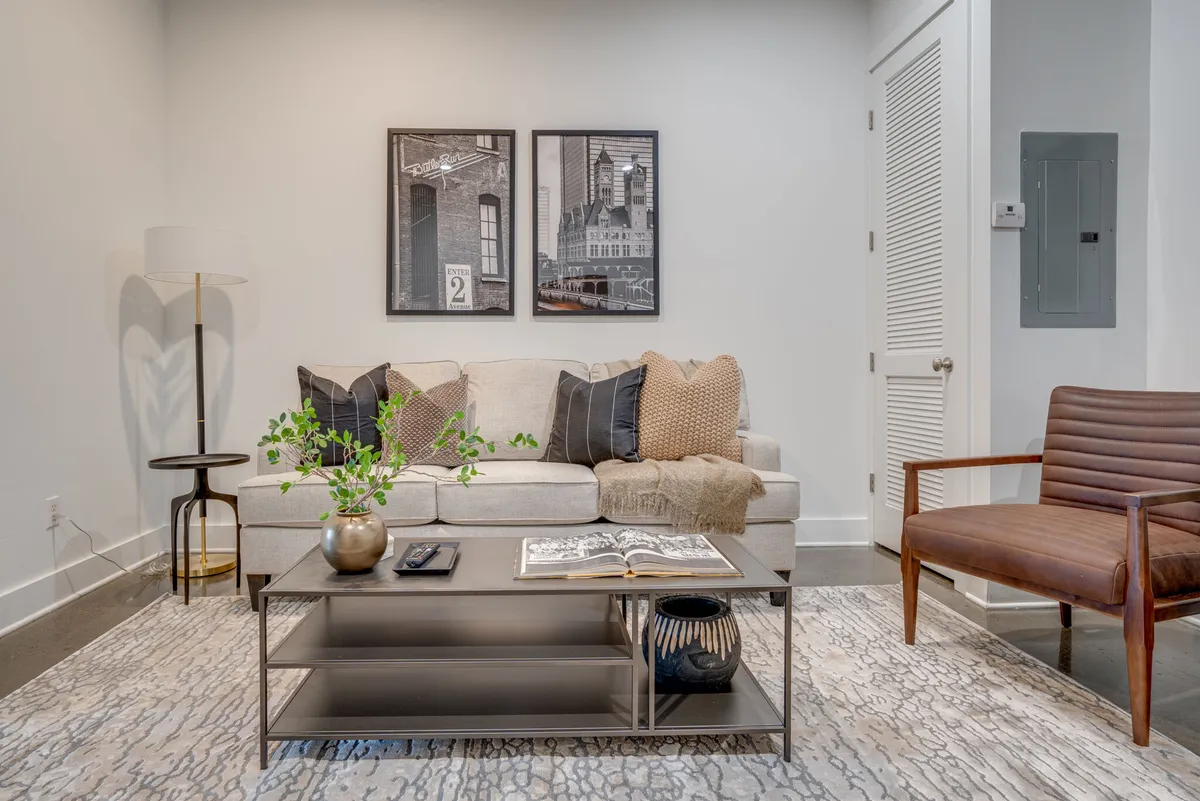 A stylish living room featuring a modern sofa with decorative pillows, a chic coffee table adorned with decor items, wall art showcasing cityscapes, and a standing floor lamp. The space exudes comfort and sophistication, serving as a welcoming entry point to the penthouse suite.