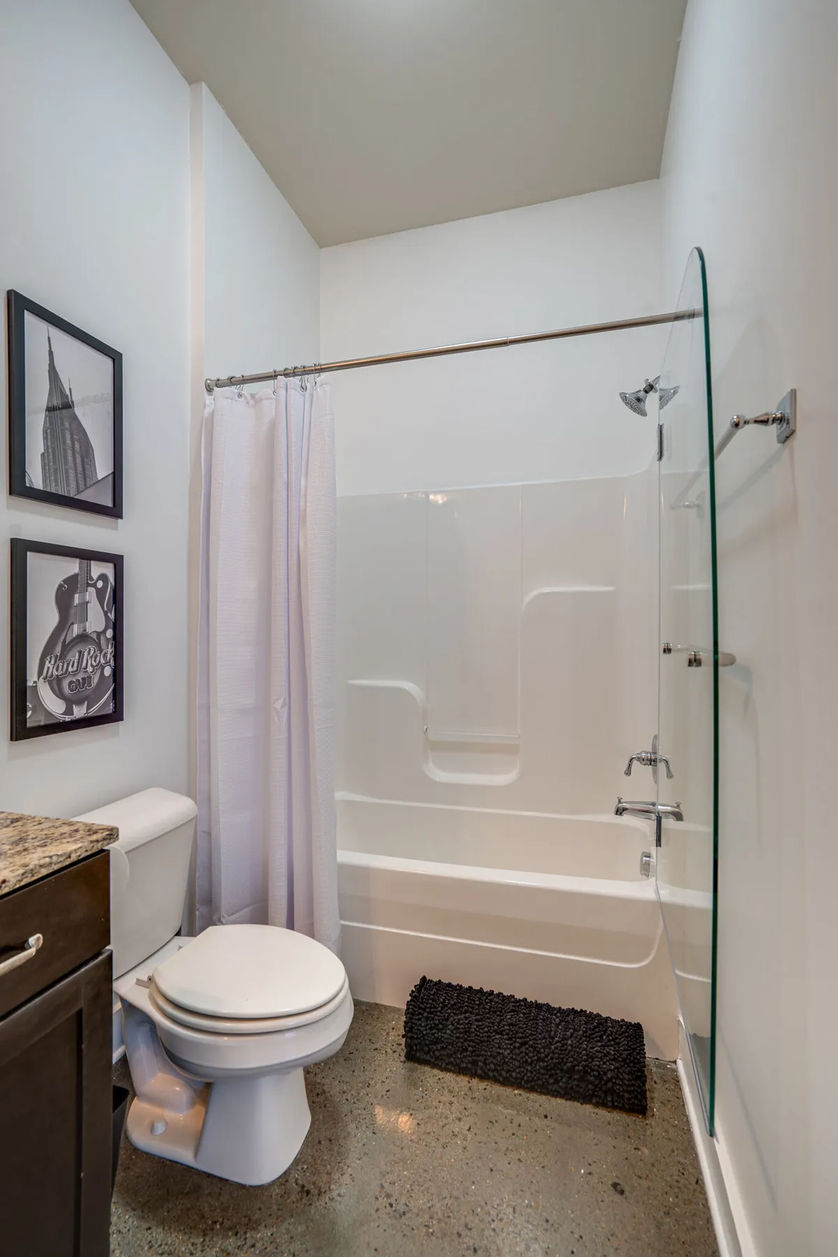A bright, minimalistic bathroom featuring a bathtub, toilet, and tasteful framed wall art. The clean lines and soothing decor evoke a spa-like, refreshing environment—perfect for personal grooming and relaxation after a long day.